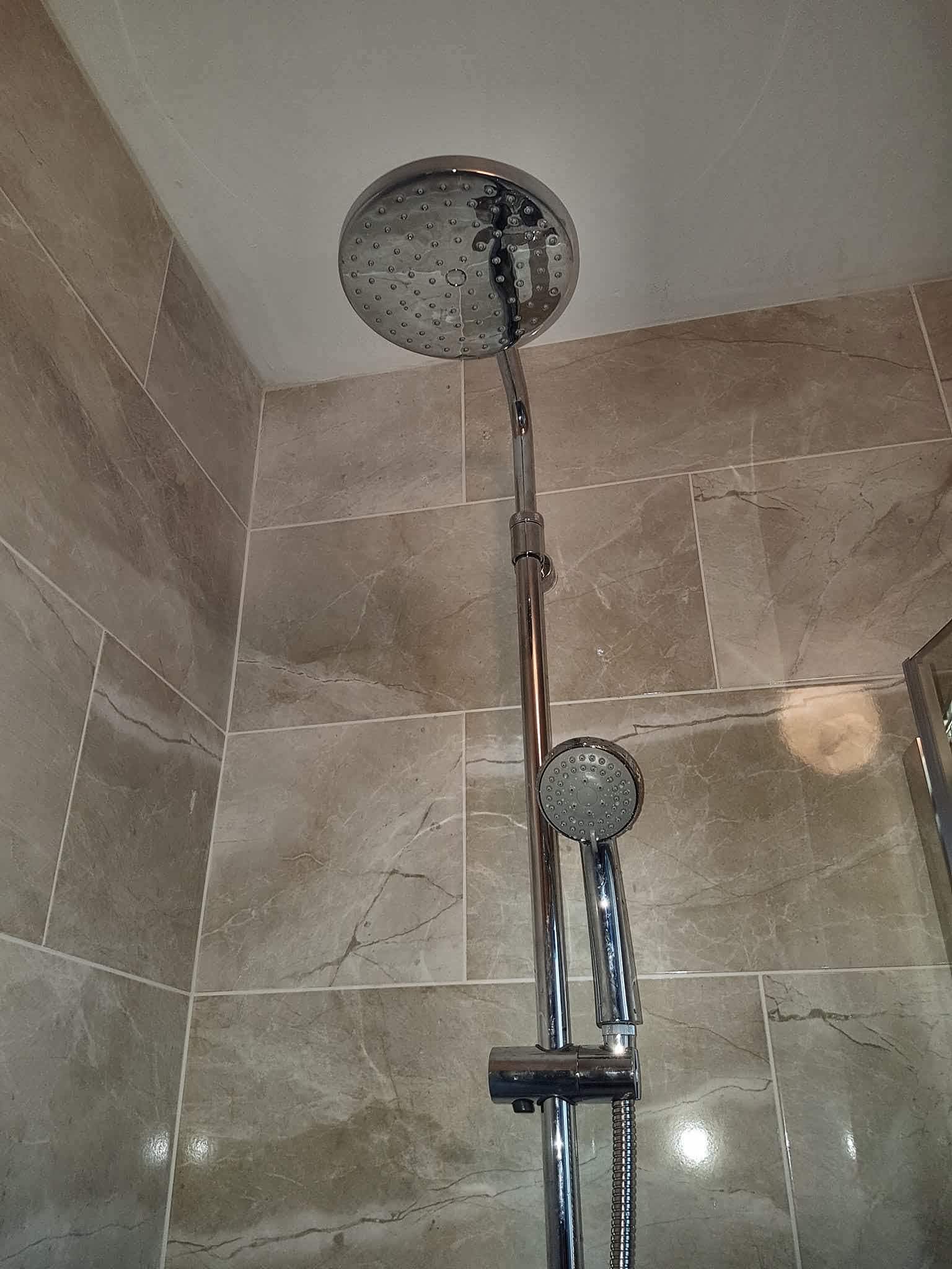 Rain shower head and handset on a tiled shower wall